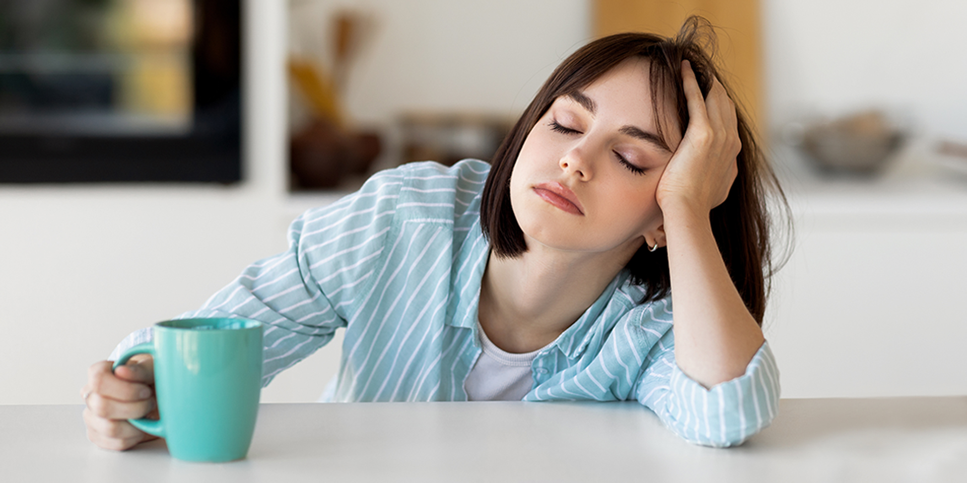 Woman falling asleep next to a cup of coffee.