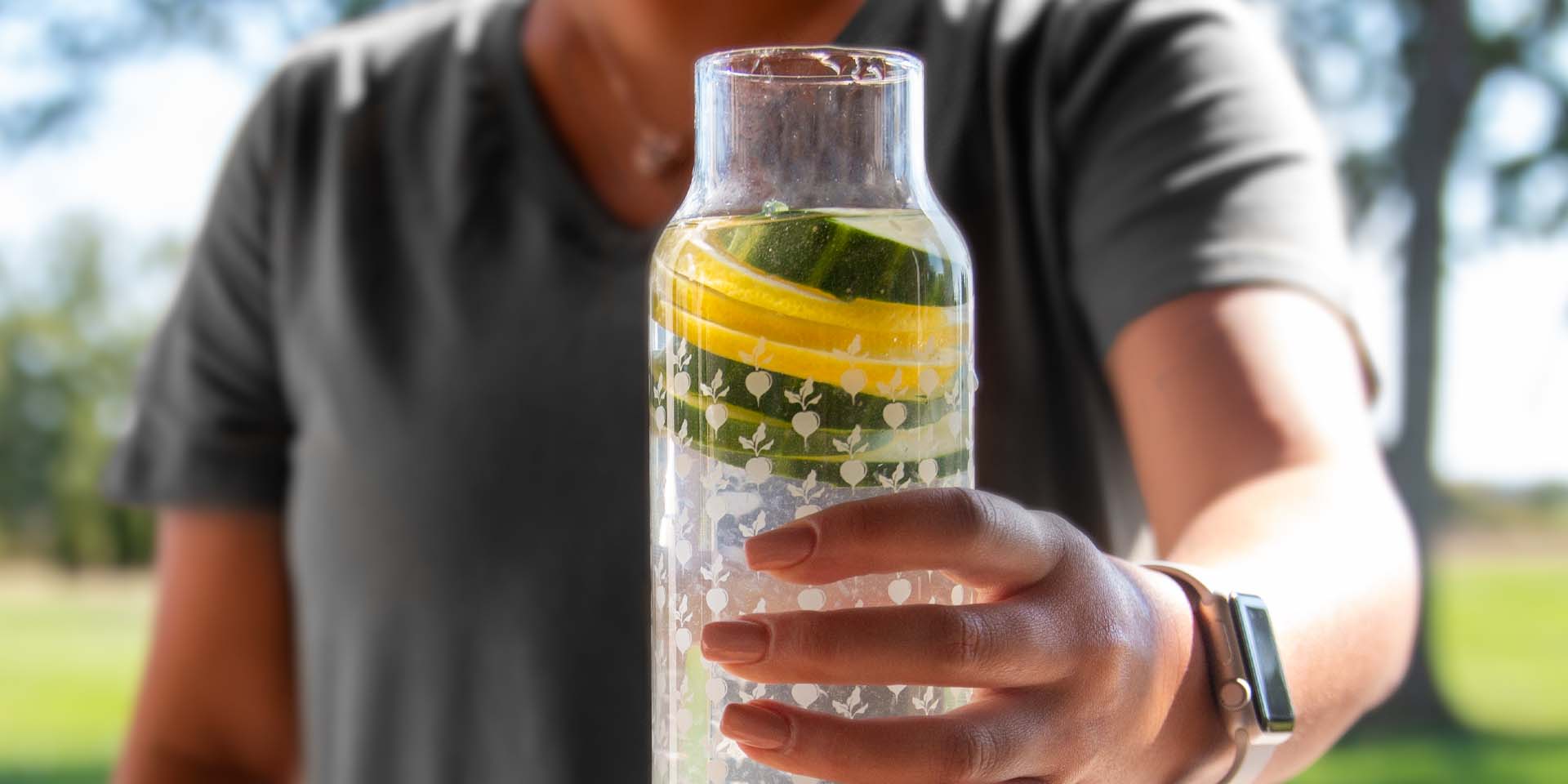 Person holding glass of water with lemons and cucumbers in it.