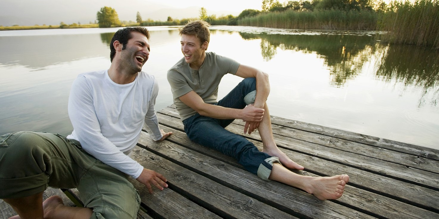 An image of two men sitting on a dock laughing together.